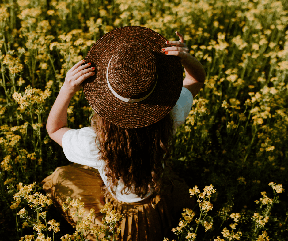 Femme portant un chapeau de paille dans un champ de fleurs sauvages, en lien avec la cueillette de plantes médicinales